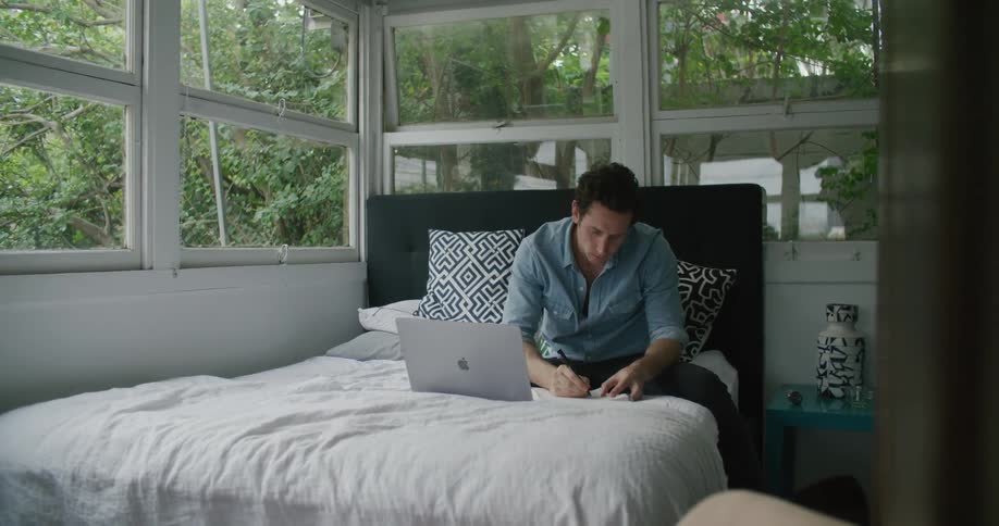 Man sitting in the bed at home working on a laptop
