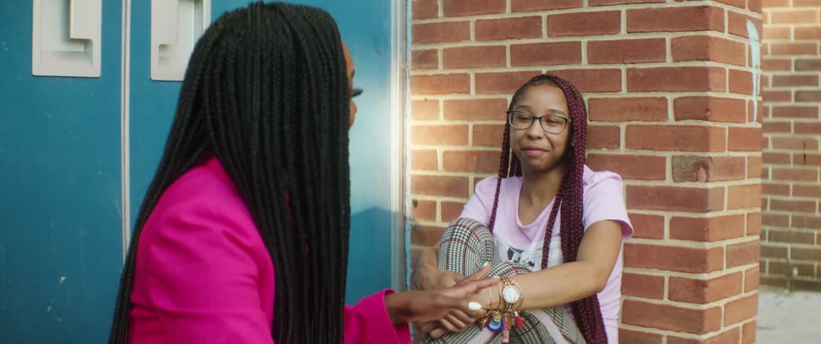 Two teenage girls sit outside a building and talk