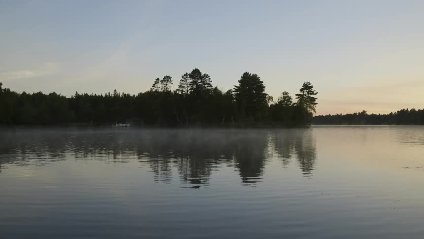 Mists linger on a calm lake at dawn