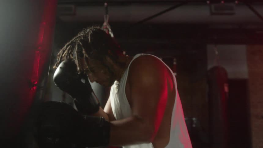 A man sweats heavily as he hits a boxing bag repeatedly in a gym
