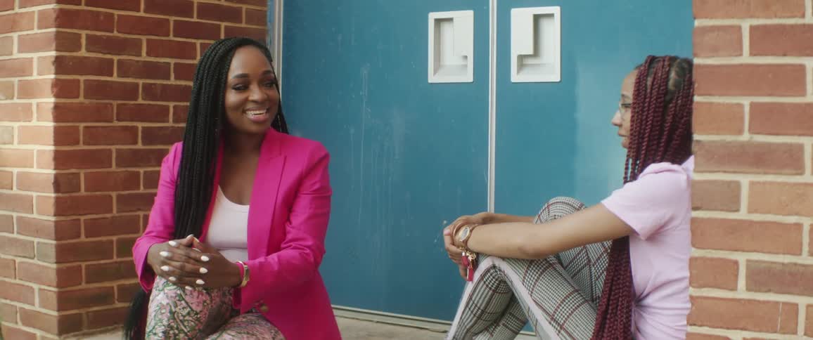 Two woman sitting and talking in front of a building with doors in the background