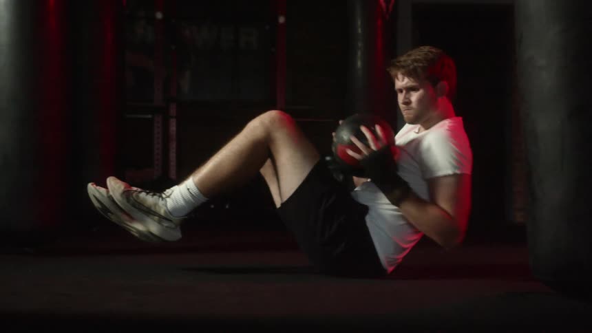 Young muscular man exercising with a weighted ball on the floor of a gym