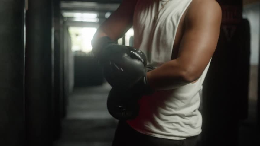 Man with braids and sleeveless white shirt wears boxing gloves to train in the boxing gym