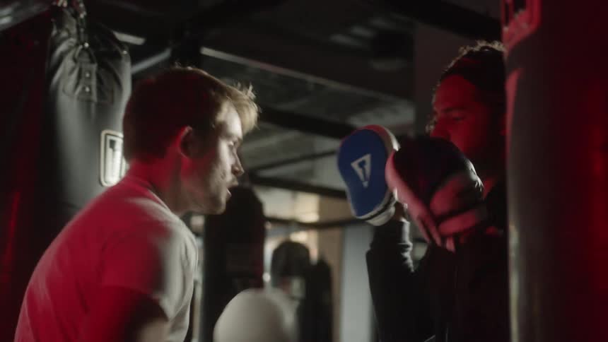 A man wearing white boxing gloves in a gym boxing with another man with safety mitts on at daytime
