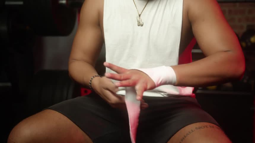 A man sitting on a bench in a gym wrapping a white wrap around his hand