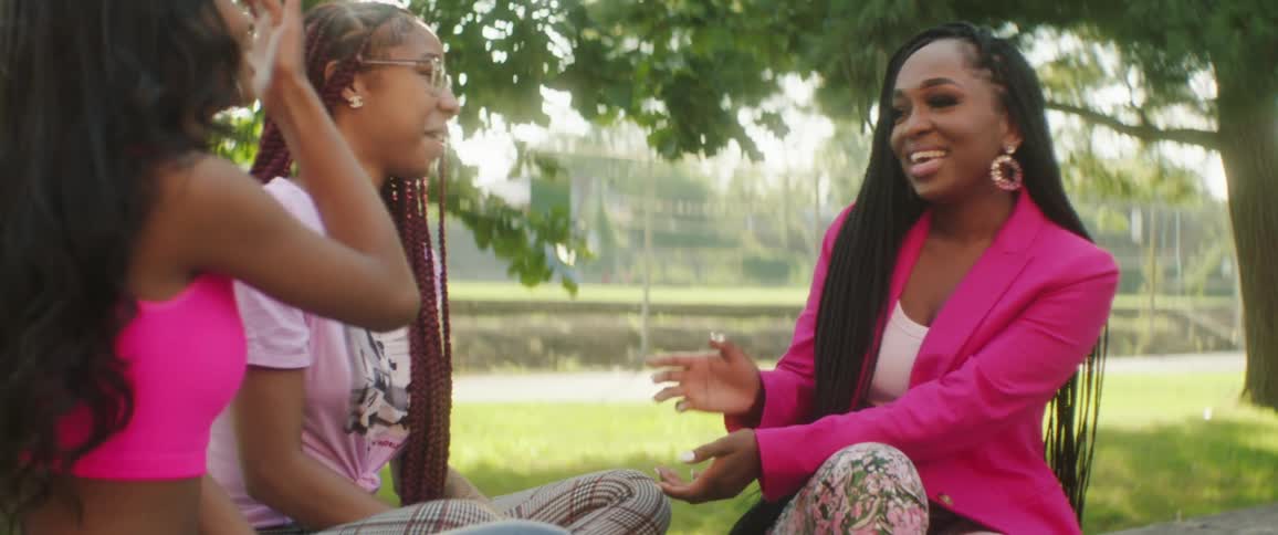 A group of women laugh while talking together outdoors on a sunny day