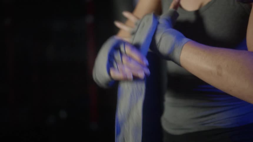 Young fit woman wrapping her hands with gray cloth bandages inside a dimly lit room