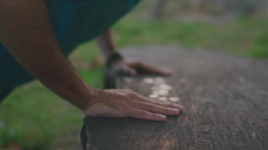 Young man doing push ups on a rock in a park at sunset