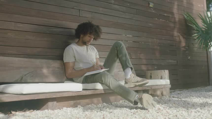 Man sits on bench writing in notebook