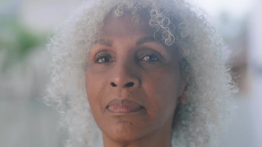 A woman with curly white hair slowly opens her eyes with a serene look on her face