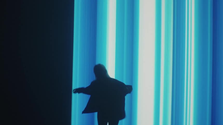Silhouette of a woman modeling in front of a giant electronic screen projected on the wall of a smoky dark room