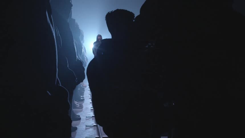 Filmmakers filming a scene with multiple extras inside a dimly lit smoky warehouse