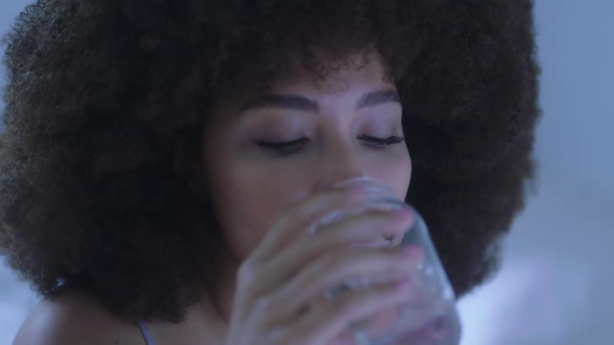 A woman in a room with make up drinking from a jar