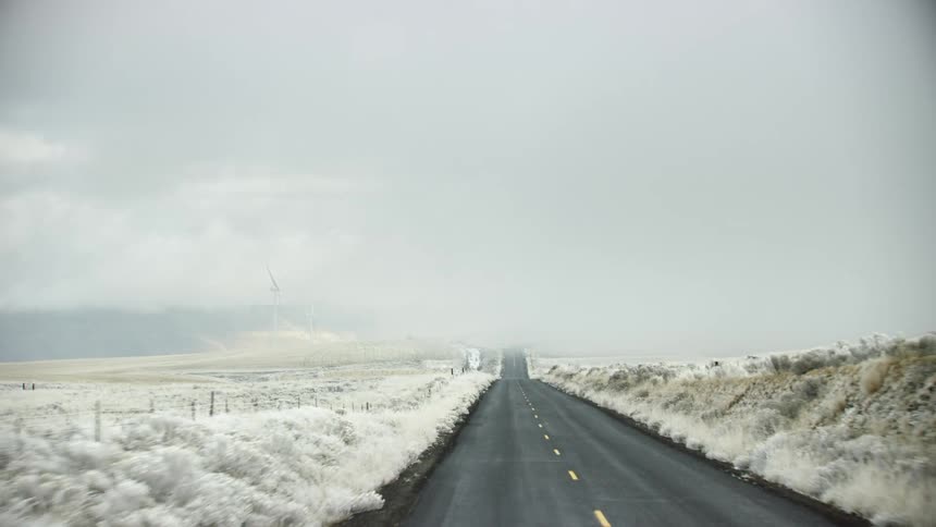Looking out the back window of a pickup truck while driving to Thanksgiving dinner down a rural country road with snow covering the dry meadow grass and sagebrush