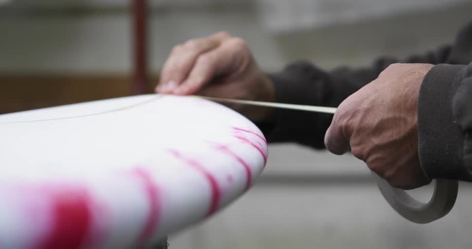 A man in a room applying tape to a surfboard with a wall in the background