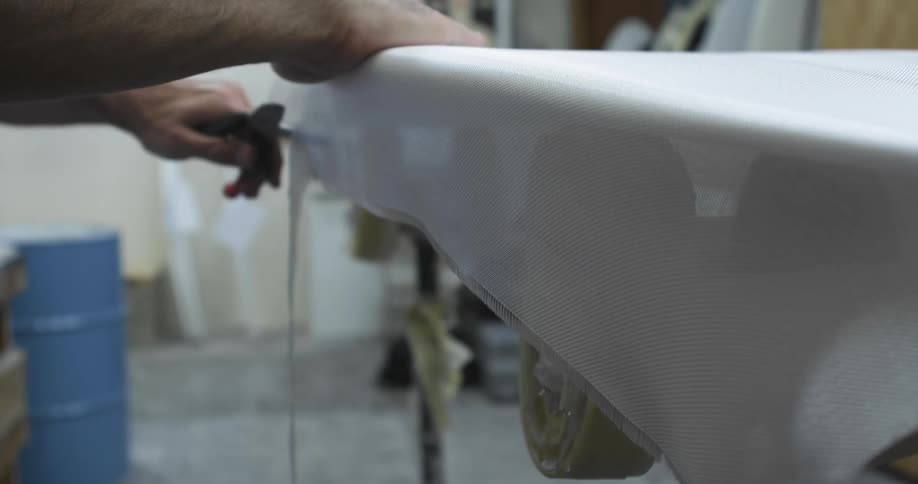 Man cutting fabric from the surface of a surfboard in a workshop