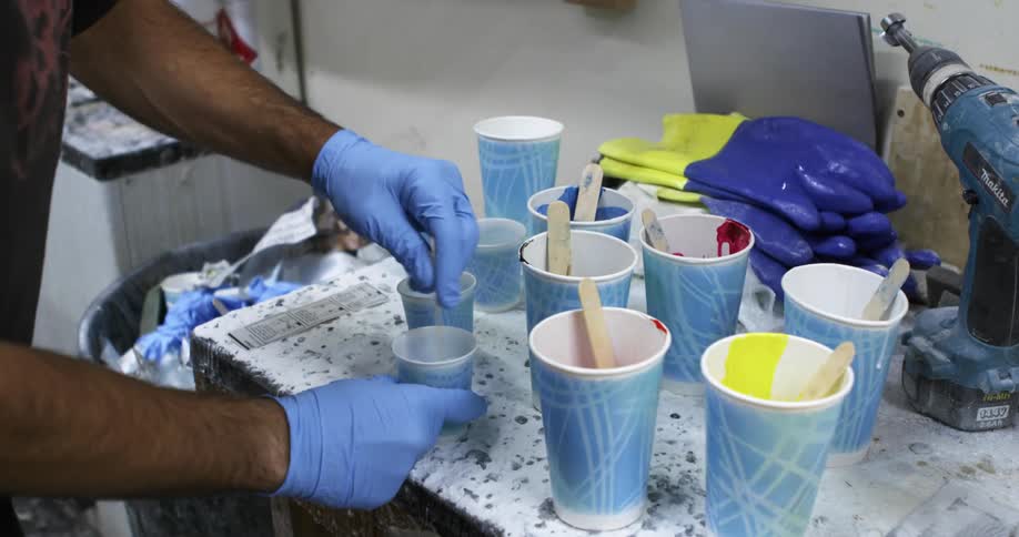 A man mixing components in plastic cups over a table inside a workshop