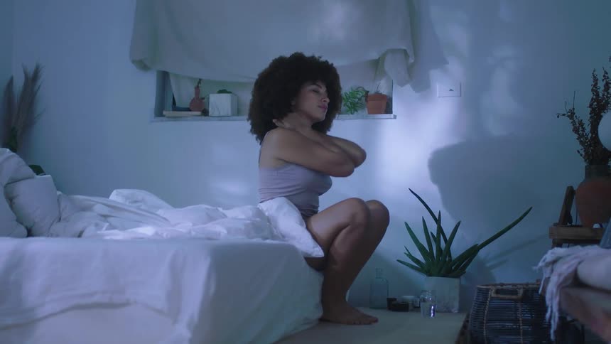 Brunette woman with frizzy hair gets up and drinks a glass of water in the bedroom