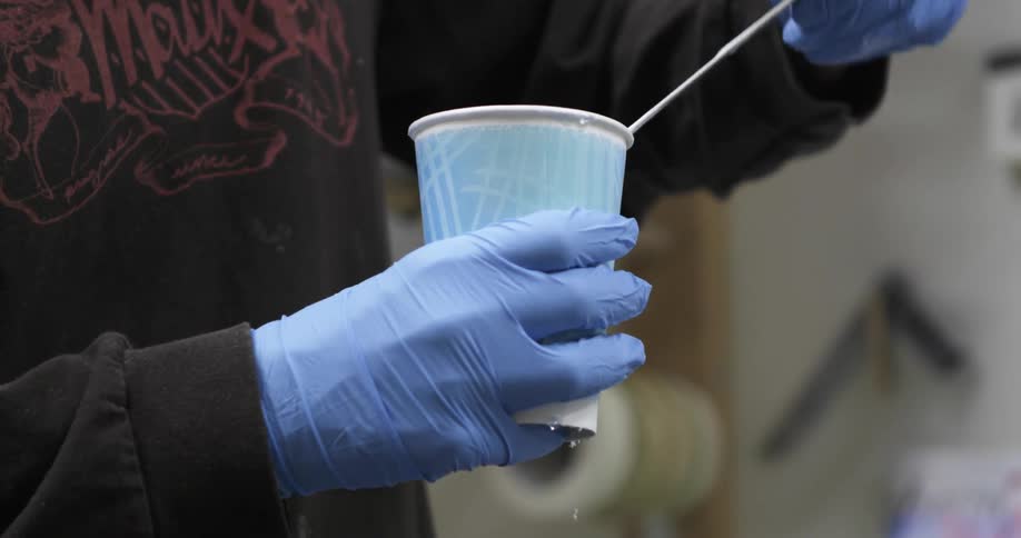 A person wearing gloves mixingplastic inside a cup