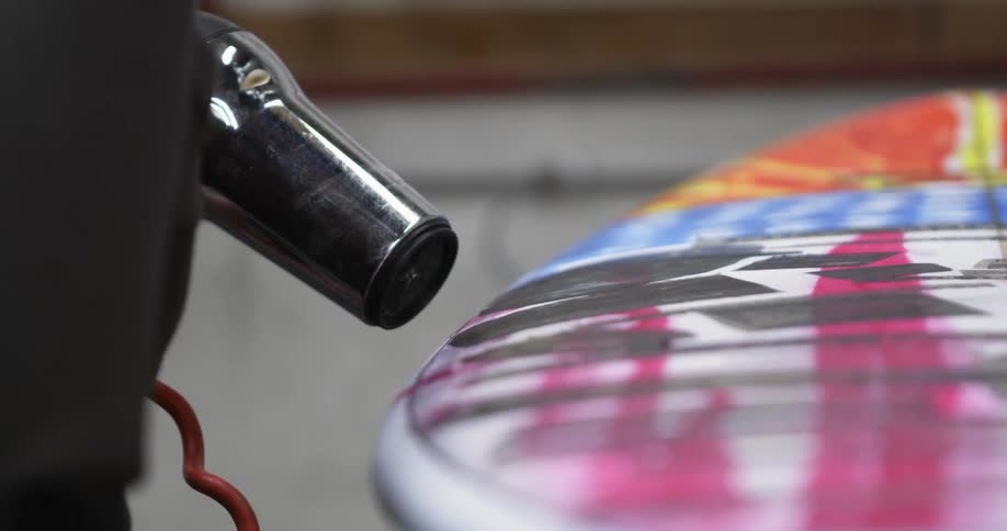 Man uses dryer to dry paints on surfboard