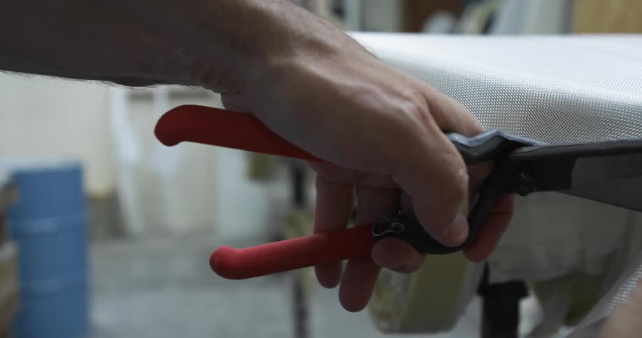 Man cutting fabric from the surface of a surfboard in a workshop