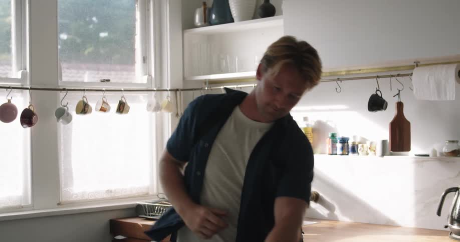 Young man picks up a bag from the kitchen coutertop and exits