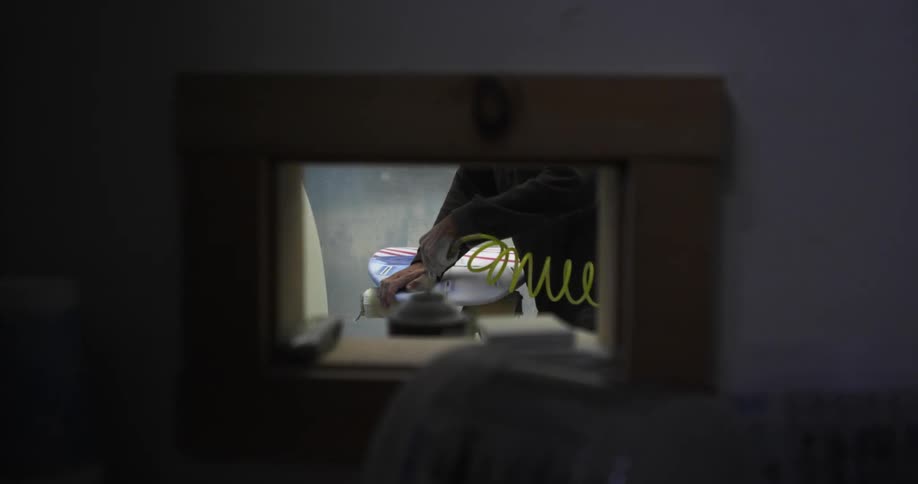 A man inside a room cleaning a surfboard using compressed air