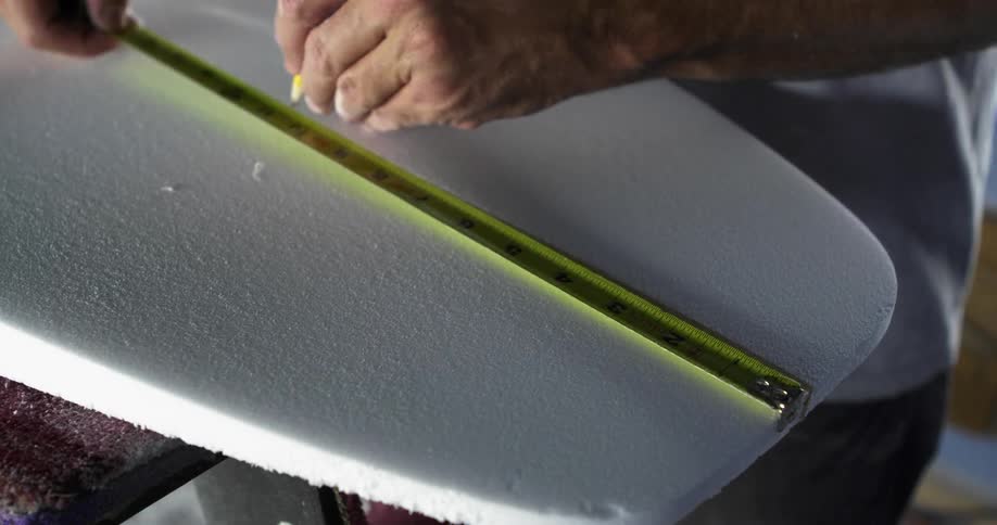 Man marks surfboard form using measuring tape