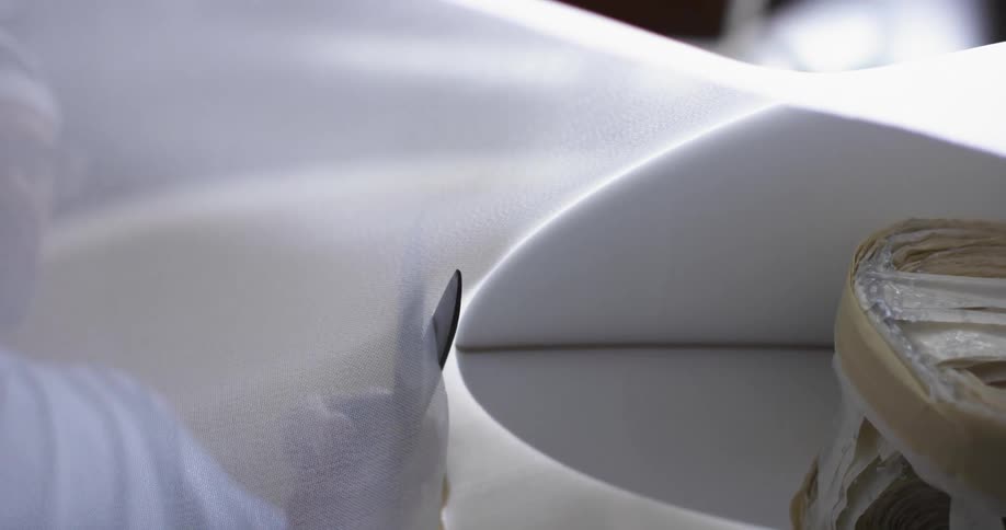 A man uses a large pair of scissors to cut a roll of fabric