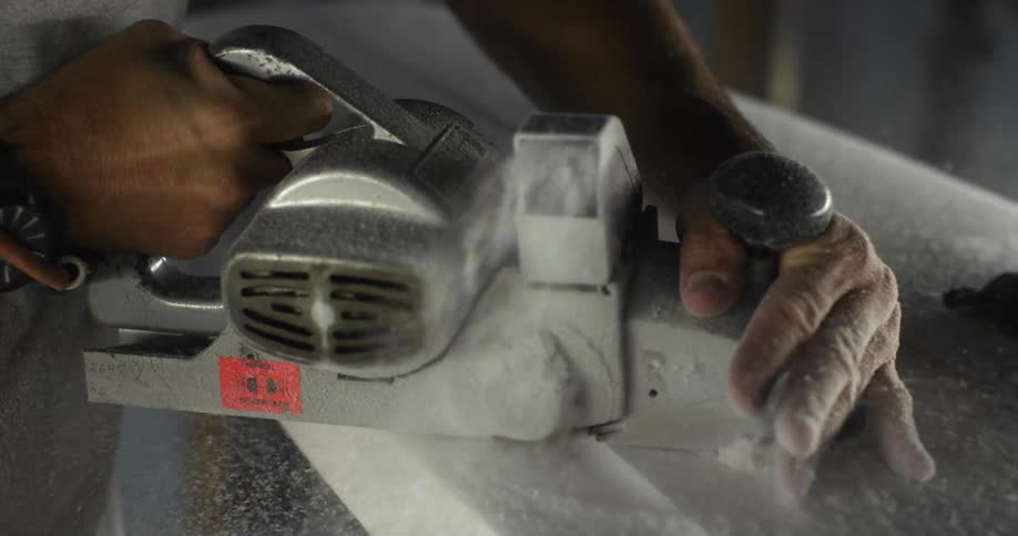 A person sanding a surfboard with an electric sander