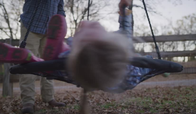 A father spins his two daughters on a flat hanging swing outdoors in the evening