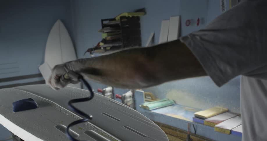 A man cleaning the surface of a surfboard in the workshop using compressed air