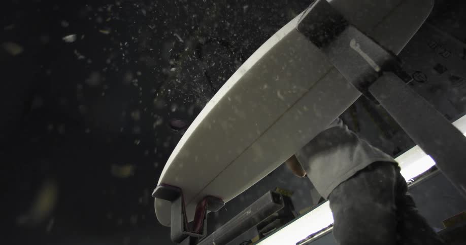 A man in a shop sands a surfboard