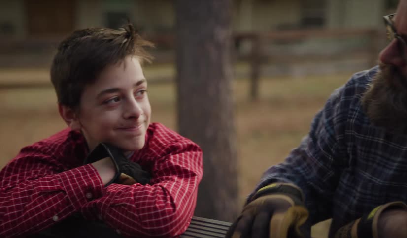 A man with glasses and gloves talking to a boy next to a fence