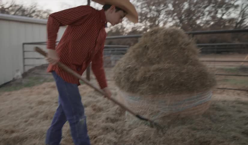 Teenage boy raking hay in a coral on a farm
