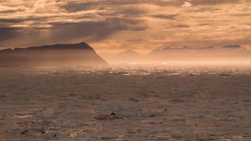 A lake with water and ice with a mountain range the sky and clouds in the background