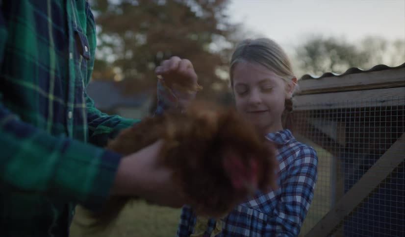 A man holds a chicken while a girl standing next to him pets it