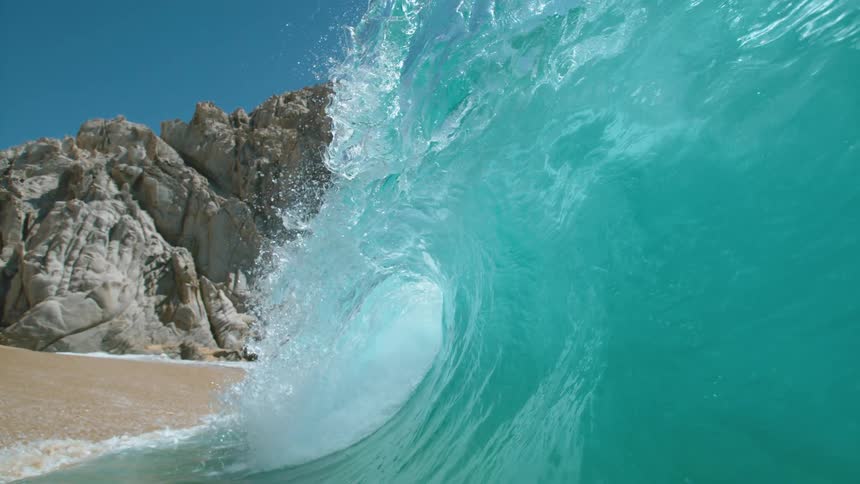 Big blue wave splashes and rolls onto a beach
