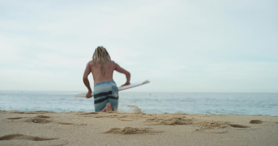 A man runs into the water with a surfboard