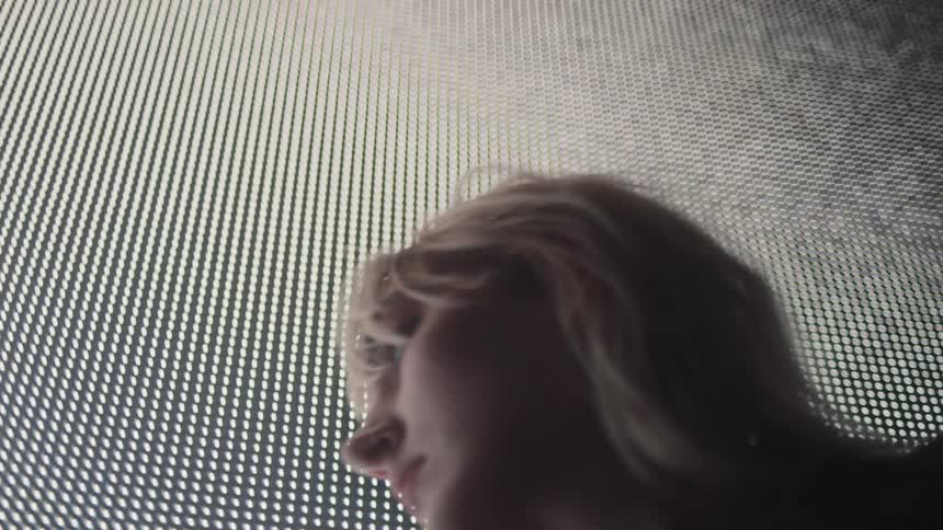 A model poses with her back pressed against a large projector screen