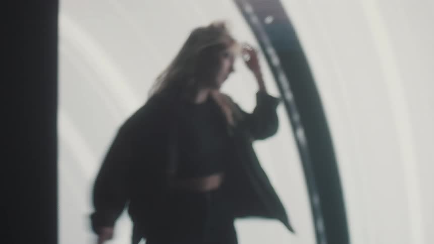 Blonde woman spins while moving back and forth in front of screen showing various images