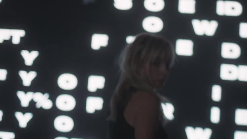 A model walks in front of a flashing sign and then turns and poses
