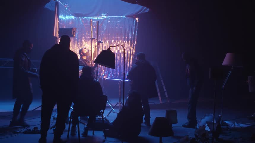 A photographer and an assistant test the light during a photoshoot in a studio with a reflective backdrop