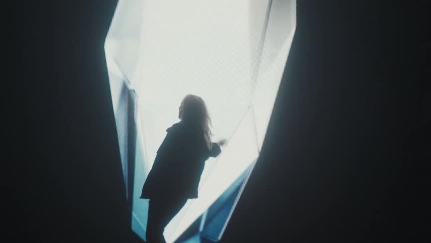 A model walks back and forth in front of a projection screen that displays a large diamond