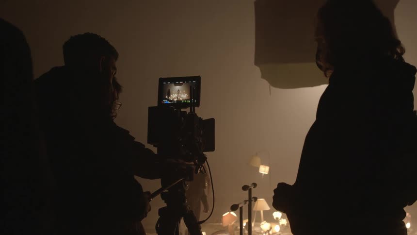 A group of people look at a camera and prepare to film a man on stage surrounded by lights