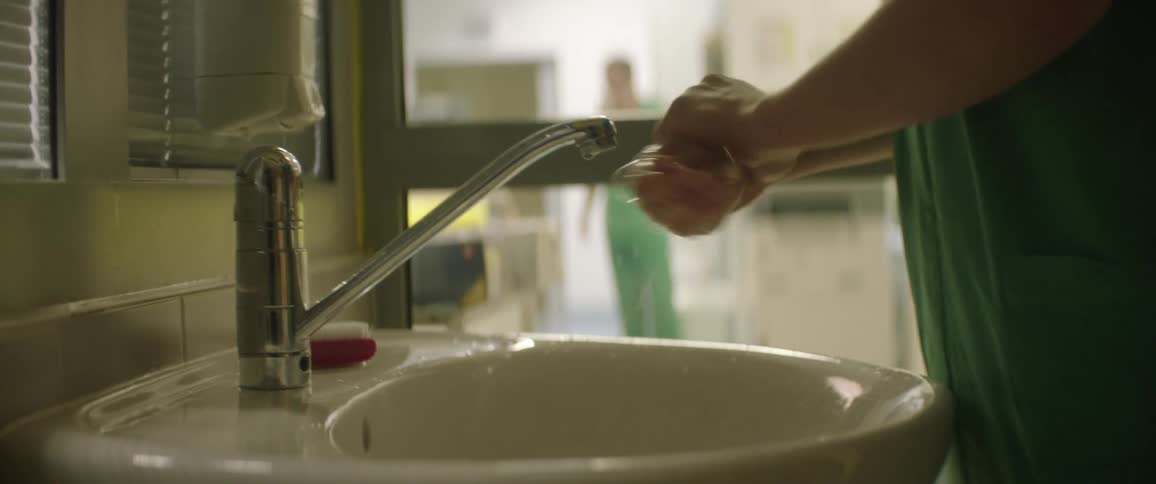 A person with scrubs in a clinic washing their hands in a sink