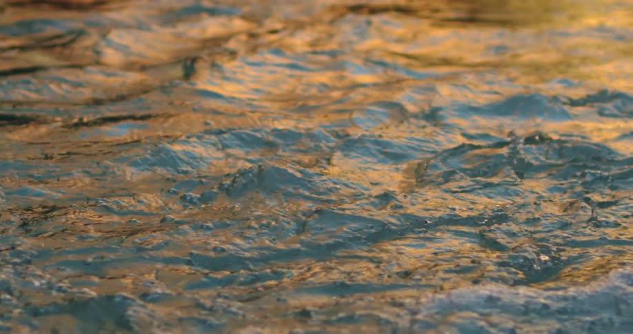 Waves ripple and flow downstream on the Colorado River deep in Grand Canyon National Park as the sunset light reflects from the sandstone walls