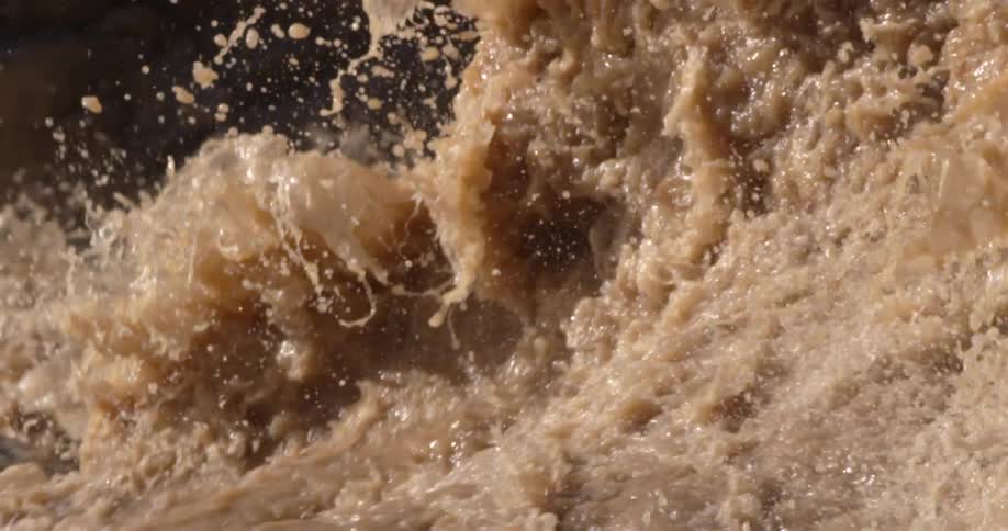 Brown spring Colorado River runoff water churns and splashes on a sunny day deep in Grand Canyon National Park in the American Southwest