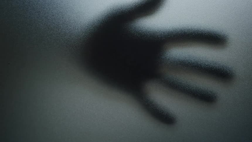 Silhouette of a hand slides across the other side of a glass