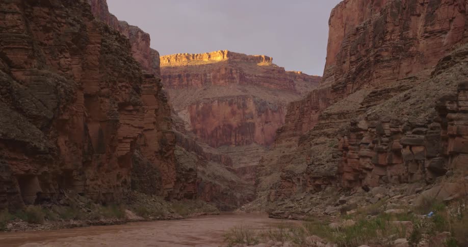 Slow tilt down from sunrise sky to a massive sandstone inner canyon at Grand Canyon National Park and the muddy Colorado River